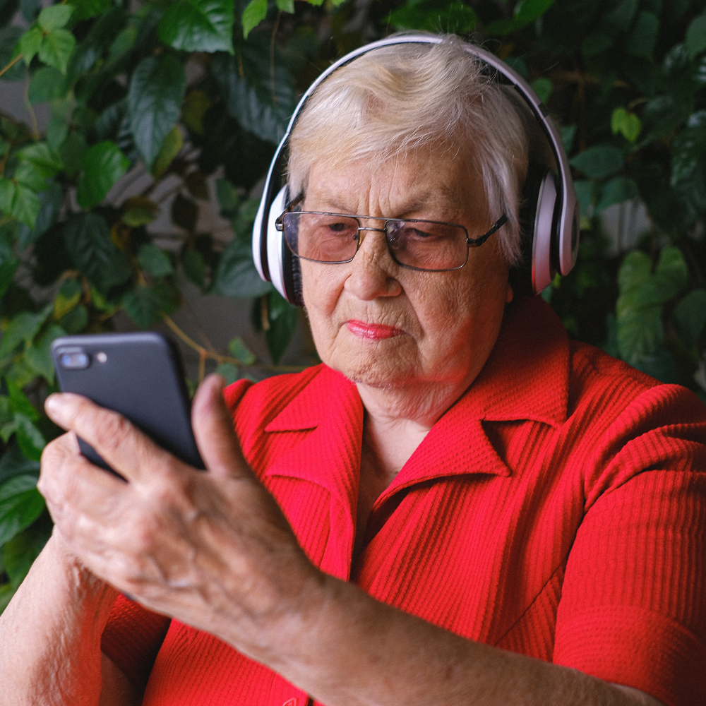 Abuela con camisa roja y cascos sujetando un smartphone