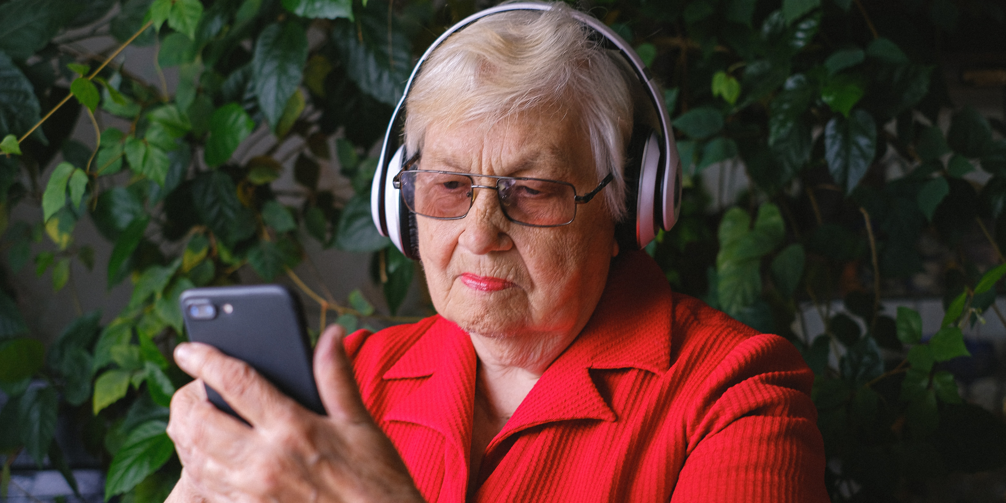 Abuela con camisa roja y cascos sujetando un smartphone